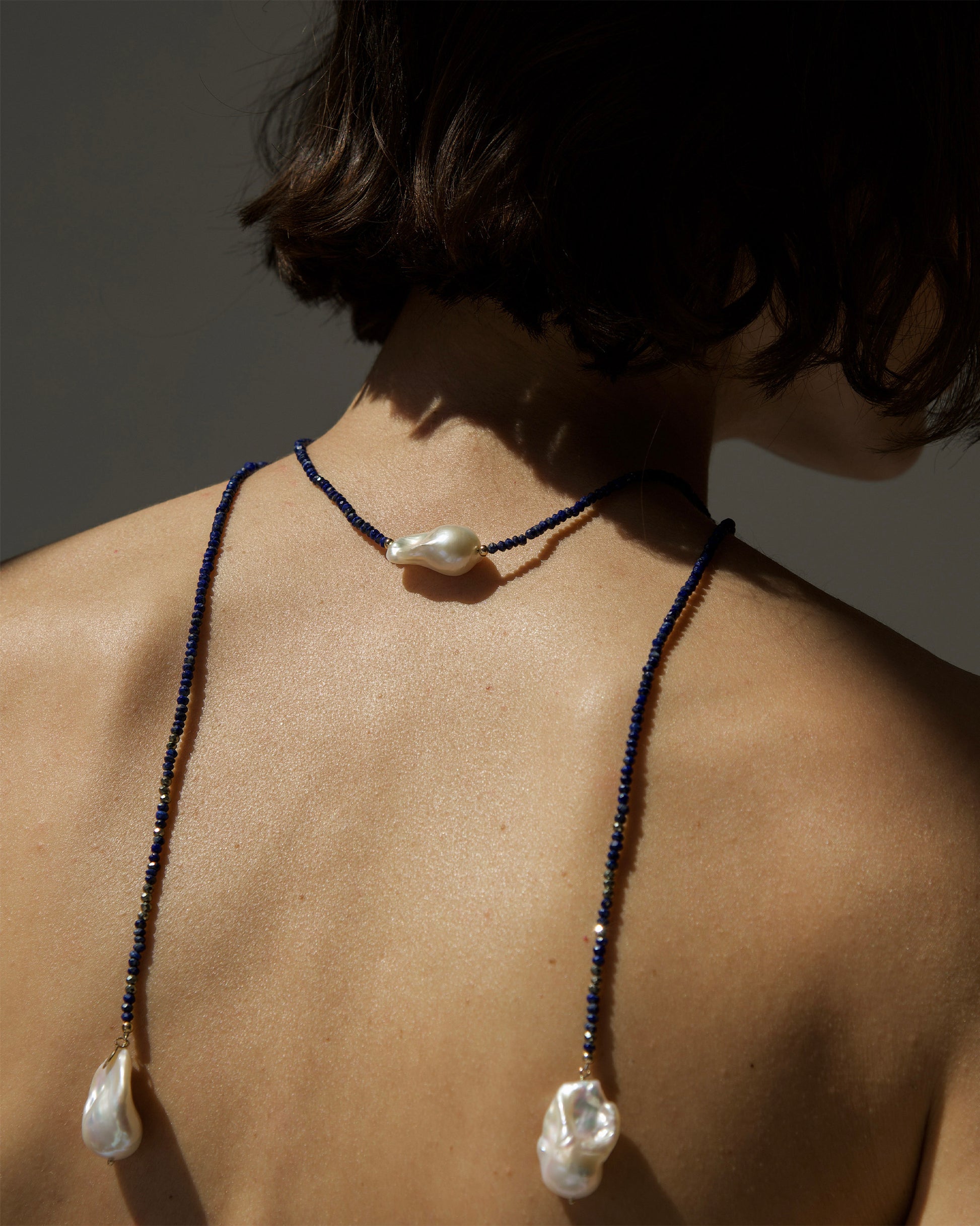 monái necklace draped over décolleté – elegant layering of baroque pearls, lapis lazuli, and pyrite for a statement look